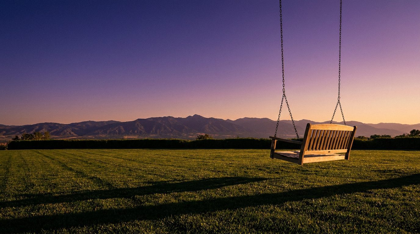 Empty wooden swing swaying gently at golden hour with mountain silhouette in the background