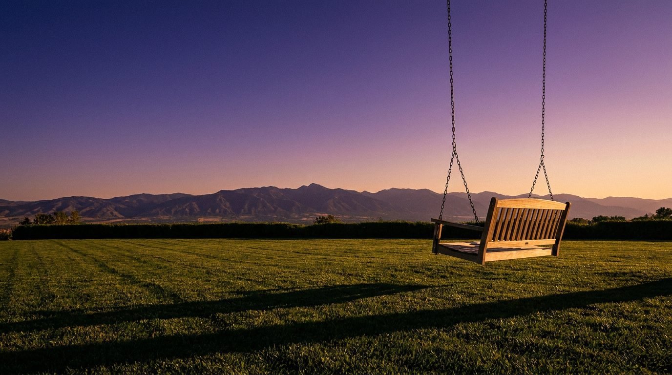 Empty wooden swing swaying gently at golden hour with mountain silhouette in the background